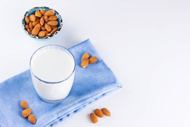 Almond milk with almond on white background. Organic almond milk in a glass for healthy breakfast. Vegan milk from almonds nuts on a blue napkin. Alternative milk - Foto, Imagem