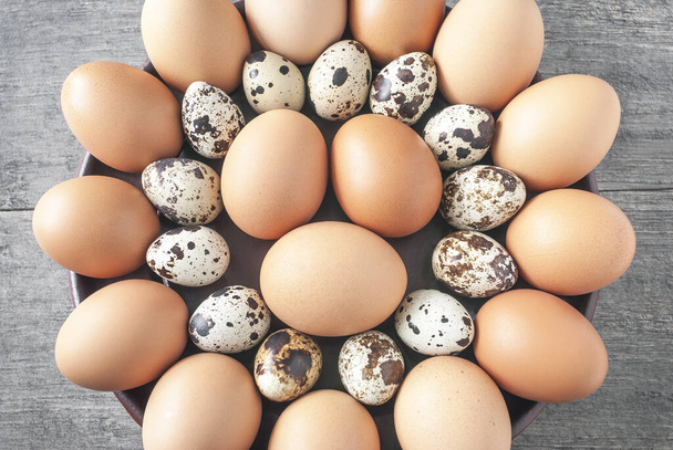 Os ovos de galinha e codorna são dispostos em fileiras na forma de uma bandeja preta em um círculo e colocados em uma bancada cinza rústica.
. - Foto, Imagem