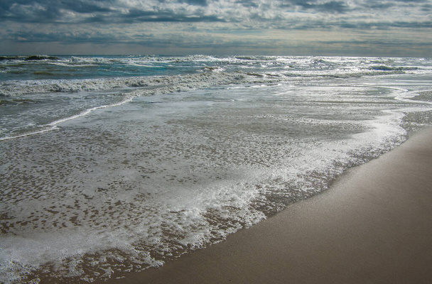 Cambiare marea: le onde in arrivo coprono la spiaggia mentre un cielo scuro inizia a schiarirsi al Capo Hatteras National Seashore
. - Foto, immagini