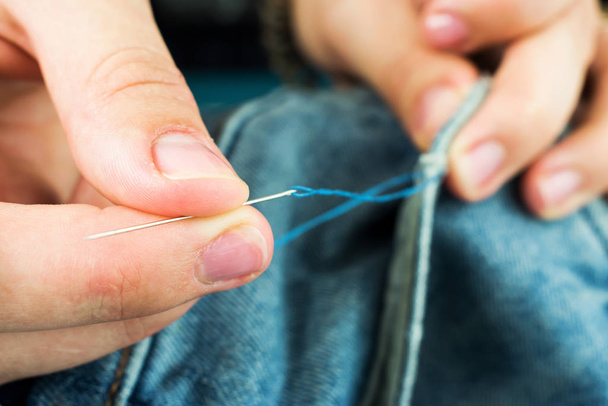 Girl sews jeans with a needle. The girl's hands holding a needle for sewing. - Foto, Imagem