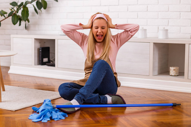 Image of  overworked housewife with mop shouting while sitting in the living room. - Fotoğraf, Görsel