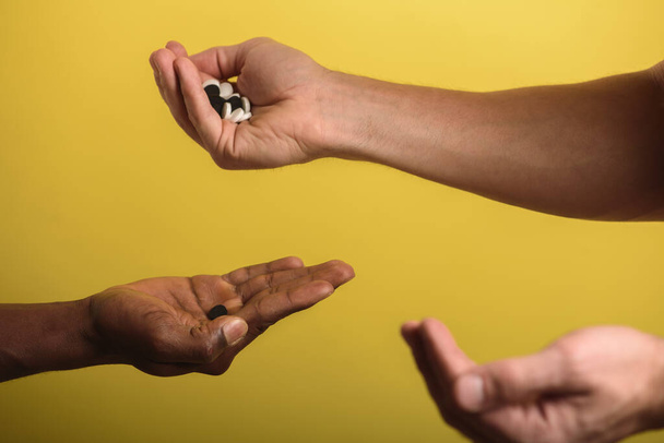 two male hands one black male second European man holding and flipping pills white and black  - Foto, imagen