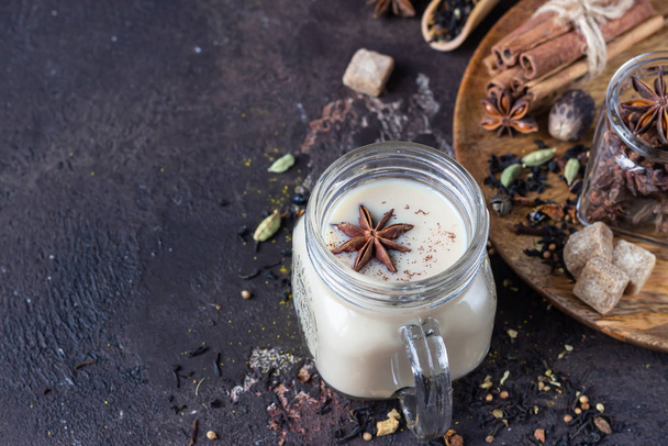 Mason jar with traditional Indian masala chai tea on dark stone background. Spiced hot tea with milk and spices for making tea - cinnamon, anise, cardamom, nutmeg, pepper and brown sugar. - Foto, Imagem