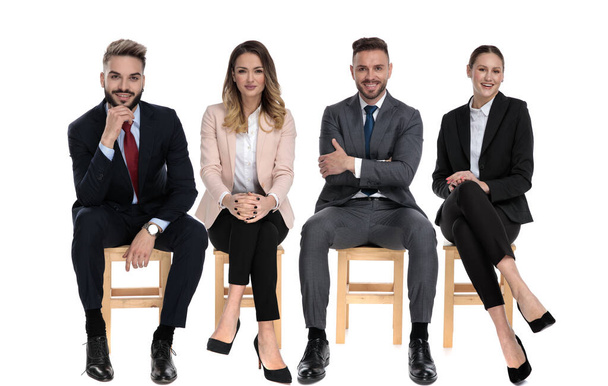 Команда из 4 позитивных бизнесменов улыбается, сидя на стульях на белом фоне студии
 - Фото, изображение