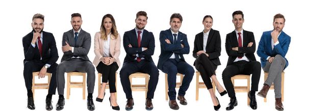 Команда из 8 уверенных бизнесменов, держащих руки скрещенными и улыбающимися, сидя на стульях на белом фоне студии
 - Фото, изображение