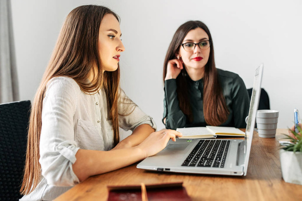 Two young girls in smart casual look at the laptop - Photo, image