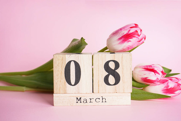 ピンクの背景に木のカレンダーとチューリップ、フラットレイアウトでクローズアップ組成。3月8日 - 写真・画像
