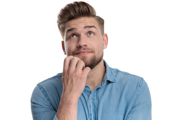 Hombre casual reflexivo mirando hacia arriba mientras usa camisa, de pie sobre fondo de estudio blanco
 - Foto, Imagen