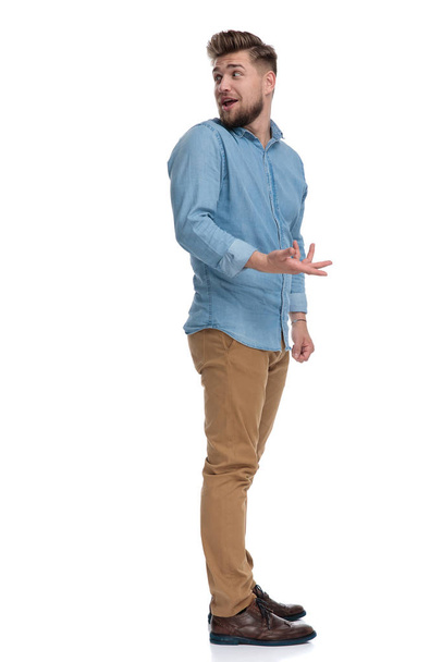 Widok z boku swobodny człowiek wyjaśniając i gestykulując, stojąc na białym tle studio - Zdjęcie, obraz
