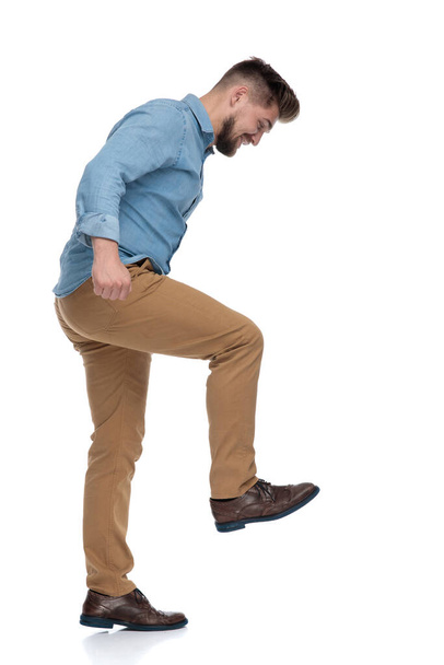 Side view of a young casual man stepping and laughing on white studio background - Photo, Image