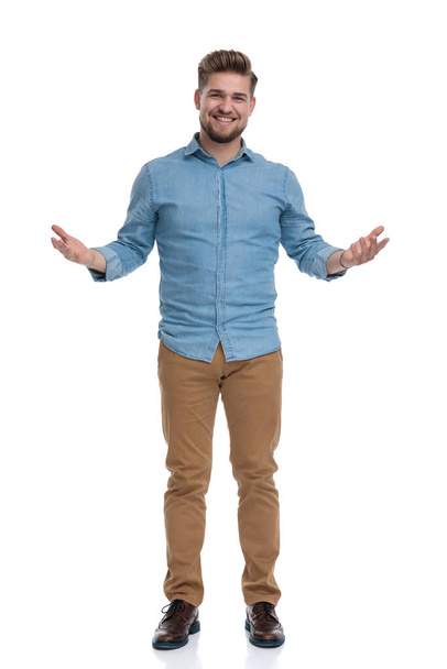 Cheerful casual man welcoming and smiling with his hands wide open while standing on white studio background - Photo, image