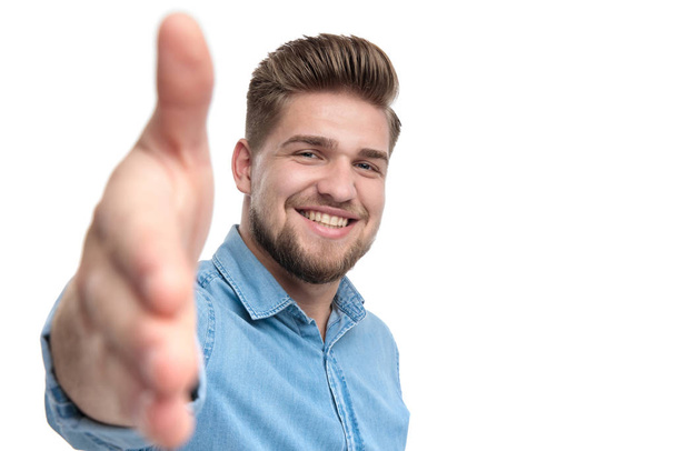 Cheerful casual man smiling and reaching for a handshake, standing on white studio background - Фото, зображення