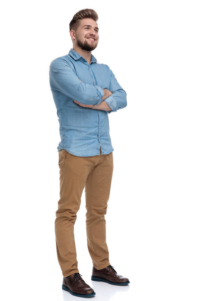 Hopeful casual man looking away with his hands crossed at his chest while standing on white studio background - Foto, afbeelding