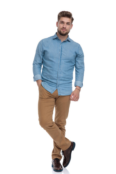 Charming casual man posing with his hand in his pocket while standing on white studio background - Foto, Imagem