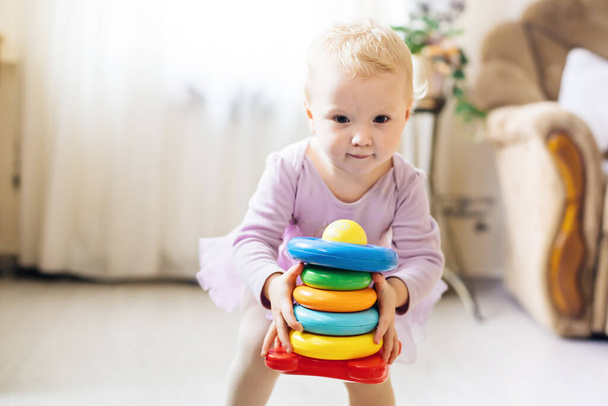 A lány logikus piramist játszik a padlón a nappaliban a napsütéses napon. Montessori fa játék hajtogatott piramis. Kör, quadra, háromszög, téglalap alakú gyermekjátékok faelemei. Többszínű játék kék, sárga, piros, zöld - Fotó, kép