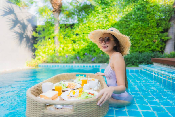 Genç Asyalı kadının portresi mutlu bir gülümseme ile otel havuzunda yüzen kahvaltı tepsisinin keyfini çıkar. - Fotoğraf, Görsel