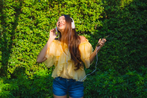 Jeune femme asiatique utilisant un téléphone portable intelligent avec casque pour écouter de la musique autour du jardin extérieur vue sur la nature
 - Photo, image