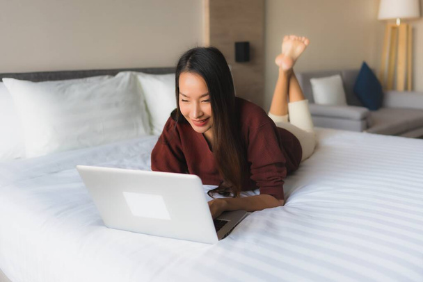 Muotokuva kaunis nuori aasialainen naiset käyttävät tietokonetta ja matkapuhelinta sängyssä makuuhuoneessa sisustus - Valokuva, kuva