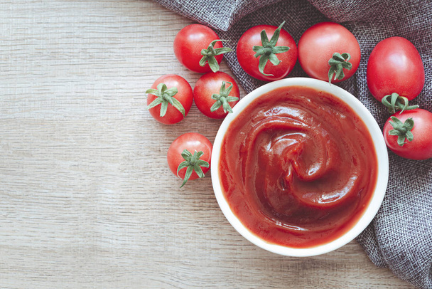 Томатний кетчупний соус в керамічній мисці з помідорами на дерев'яному фоні
. - Фото, зображення
