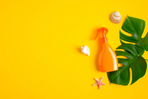 Sunscreen spray lotion orange bottle, green tropical leaves, seashells on yellow background. Sun protection and skin care concept. Flat lay, top view - Fotografie, Obrázek