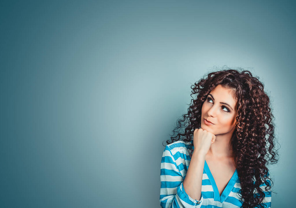 Daydreaming, thinking. Young beautiful playful curly woman with cunning tricky glance smiling looking up to left side over blue background. - Photo, Image