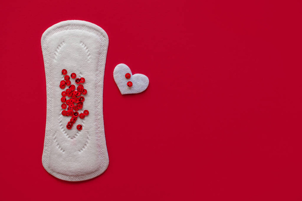 Menstrual pad with red sparkles in the shape of a heart on a red background, free space for text, the concept of menstruation in women, a tool for stopping blood during the menstrual cycle - Photo, Image