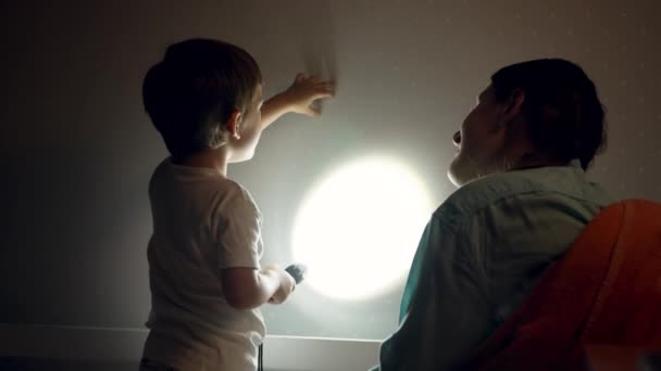 4k-Video des kleinen lächelnden Jungen und der jungen Mutter mit Schattenspiel an der Schlafzimmerwand vor dem Schlafengehen - Filmmaterial, Video