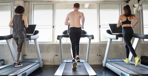 Rear view image of a sporty caucasian people group in sportswear exercising with running machine in fitness gym - Photo, Image