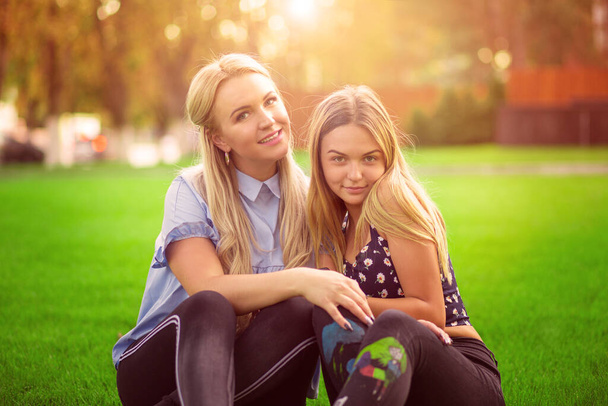 Daughter and mother concept. Young pretty girl hugging posing with her mom in a park near house on a grass loan outside sunny background - Foto, Imagen