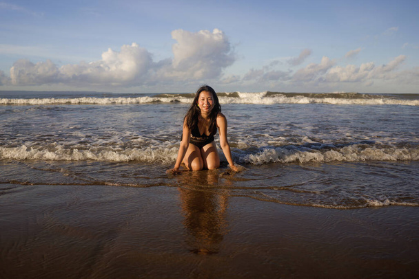 natural lifestyle portrait of young attractive and happy Asian Chinese woman in swimsuit kneeling on sand at beautiful beach paradise feeling relaxed and cheerful enjoying holidays carefree  - Фото, изображение