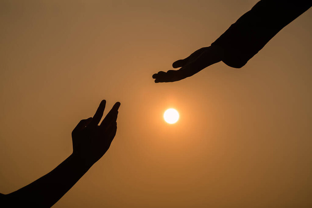 Dar una mano de ayuda en el fondo de la puesta de sol. Silueta de ayudar concepto de la mano y el día internacional de la paz
.  - Foto, imagen