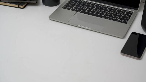 Gehakte opname van minimale werkruimte met laptop, smartphone en kopieerruimte op witte tafelachtergrond - Foto, afbeelding
