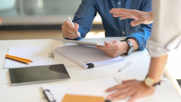 Vista de perto de dois homens de negócios informando sobre seu trabalho com tablet e arquivo de documentos na mesa branca na sala de reuniões simples
 - Foto, Imagem