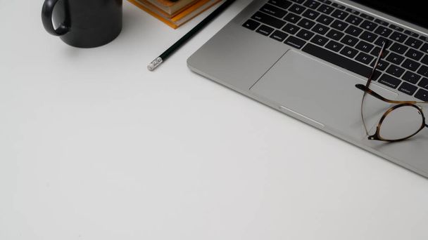 Gehakte opname van minimale werkruimte met laptop, bril, briefpapier en kopieerruimte op witte tafelachtergrond - Foto, afbeelding
