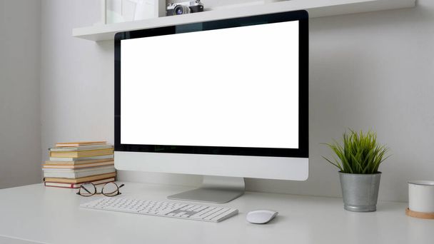 Обрізаний знімок мінімального робочого простору з порожнім екраном, книги та прикраси на білому столі з полицею на білій стіні
  - Фото, зображення