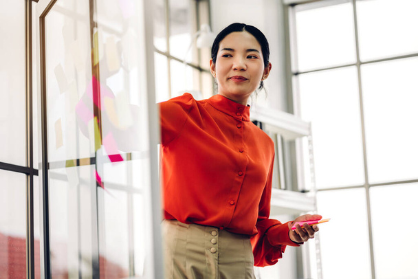 Casual επιχειρηματίας σχεδιασμό γυναίκα και γραφή brainstorm πάνω από το έργο με αυτοκόλλητα σημείωμα στο γυάλινο παράθυρο στο σύγχρονο γραφείο - Φωτογραφία, εικόνα