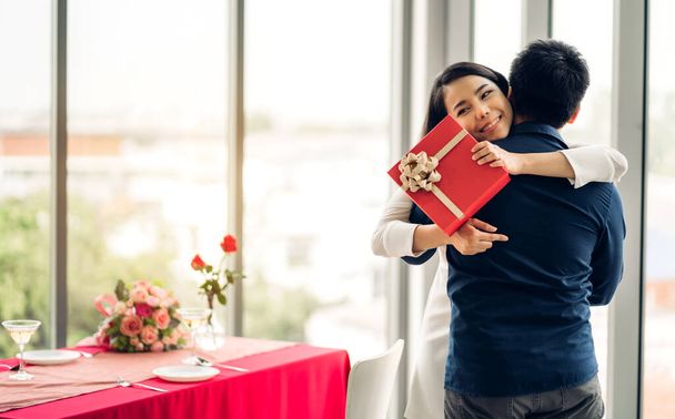 Junger schöner Mann gibt Geschenk-Box Überraschung für Freundin.Schöne lächelnde Frau umarmt Mann zu Hause - Foto, Bild