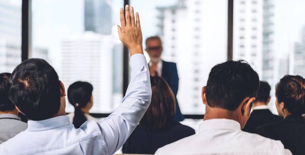 Бизнесмен, стоящий перед группой людей на семинаре консалтинговой конференции и показывающий руку, чтобы ответить на вопрос в зале или комнате семинара. - Фото, изображение