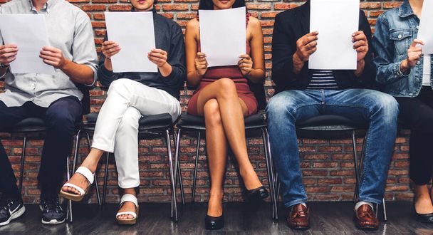 Grupo de empresarios sosteniendo papel mientras están sentados en la silla esperando una entrevista de trabajo contra el fondo de la pared
 - Foto, Imagen