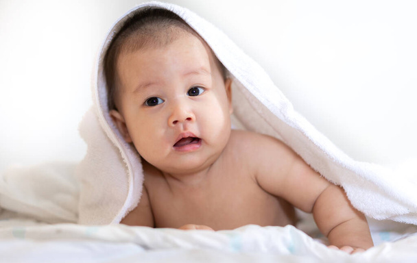 Portret szczęśliwego azjatyckiego uśmiechu dziecka relaksującego się pod ręcznikiem po kąpieli na łóżku - Zdjęcie, obraz