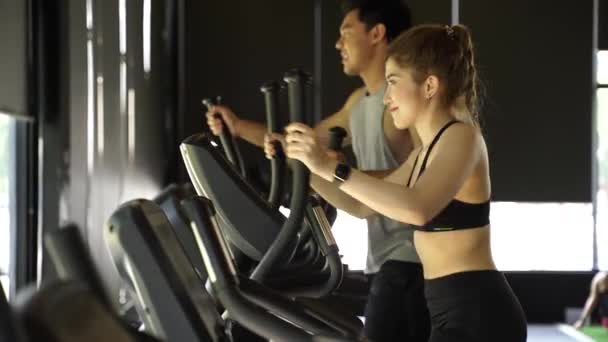 Attractive Asian fitness woman using elliptical trainer at the gym. Healthy and weight loss lifestyle - Séquence, vidéo