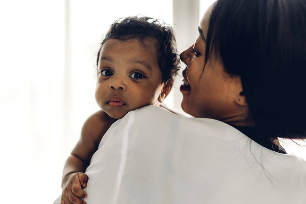 Afroamerykanka matka trzyma urocze małe afrykańskie dziecko w ramionach w sypialni.Miłość do czarnej koncepcji rodziny - Zdjęcie, obraz