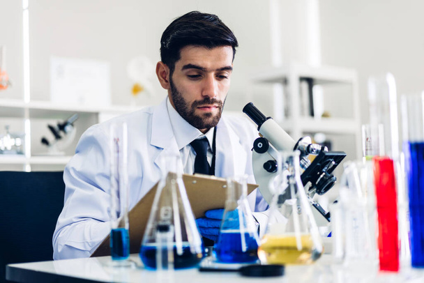 Hombre científico profesional haciendo un experimento químico mientras hace una investigación y usa microscopio con productos químicos mezclados en tubo de ensayo en el Laboratorio moderno
 - Foto, Imagen