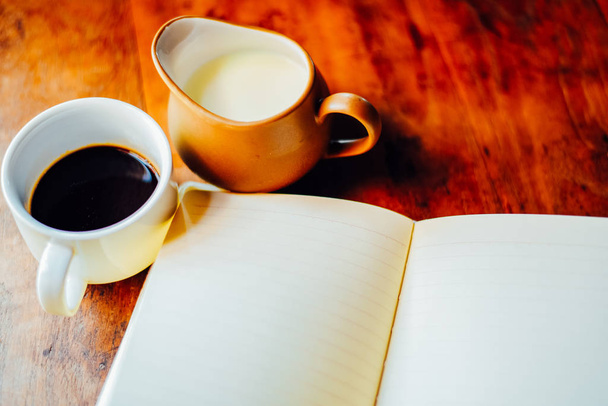 Vista superior Café quente com leite e caderno aberto em xícara branca na mesa pela manhã
 - Foto, Imagem