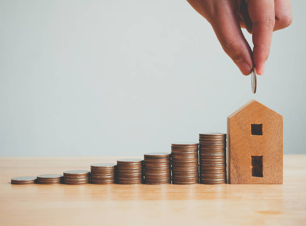 Property investment real estate and house mortgage financial concept, Hand putting money coin stack with wooden house - Photo, Image
