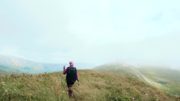 Hátulnézeti felvétel egy sporttáskás nőről és botokról, aki túrázik és egy hegyen sétál a Kaukázusban, Adygeában, Oroszországban. Fiatal nő séta a hegyekben, fitness és a testmozgás a szabadban. - Felvétel, videó