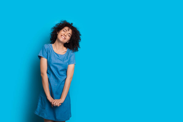 Монохромный портрет молодой кудрявой девушки, позирующей в синем платье рядом с пустым пространством
 - Фото, изображение