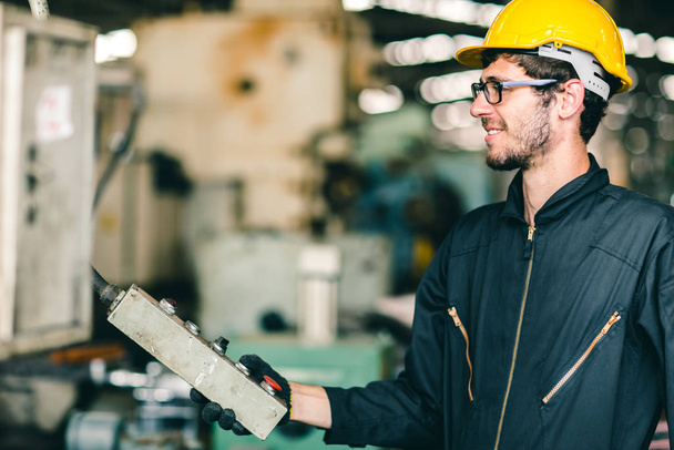 Güvenlik giysisi ve kaskı olan işçi mühendisi mutlu bir şekilde gülümsüyor ve endüstri fabrikasında ağır makineler çalıştırıyor.. - Fotoğraf, Görsel