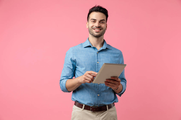 happy young guy smiling and holding tab, standing on pink background - Foto, afbeelding