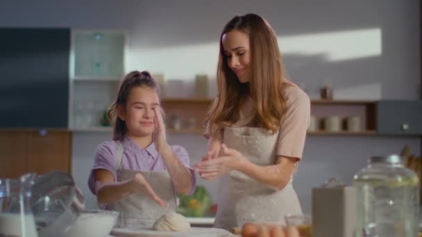 Smiling woman and girl shaking off flour on kitchen. Daughner helping mom. - Materiał filmowy, wideo